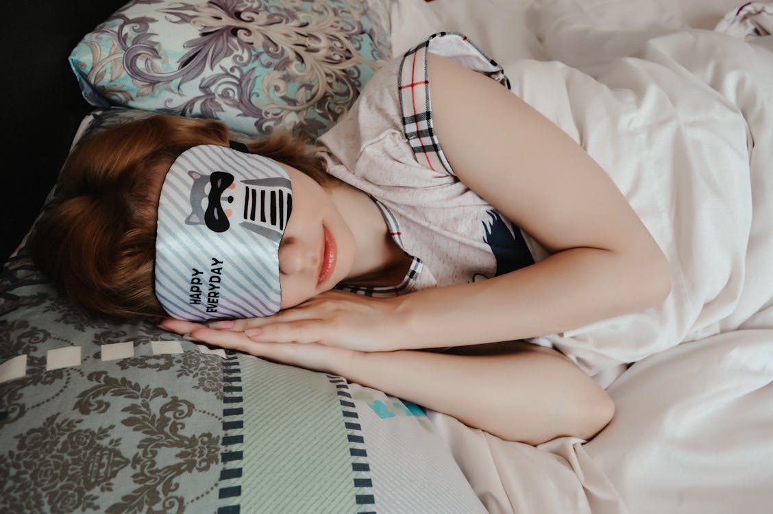 Free Anonymous female covering eyes with sleep mask taking nap while lying on bed under blanket in cozy bedroom at home Stock Photo