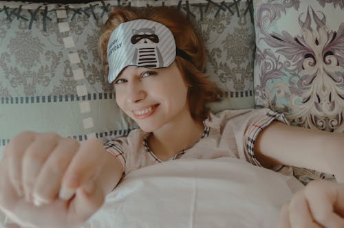 Cheerful woman with sleep mask lying on bed