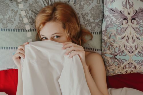 Free Top view of content female covering half face with blanket looking at camera while lying on cozy bed with pillows in bedroom at home Stock Photo