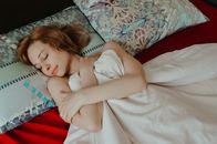 一位放松的女性双臂交叉，躺在垫着枕头的舒适床上打盹