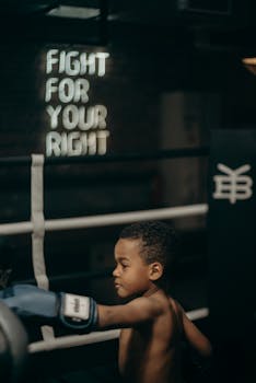 Focused young boy throws a punch in a dimly lit boxing gym with motivational text.