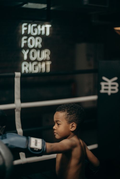 Free Focused young boy throws a punch in a dimly lit boxing gym with motivational text. Stock Photo