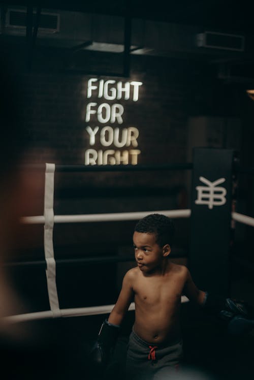 Topless Boy Sitting on White and Black Striped Textile