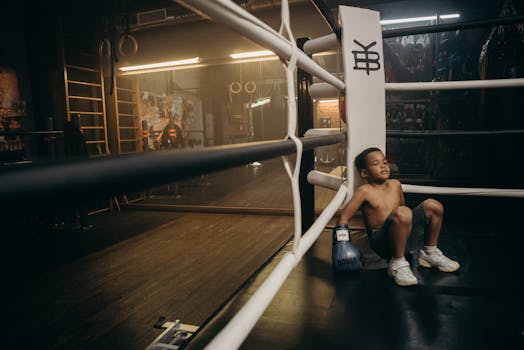 Young boy resting in a boxing ring after intense training session.