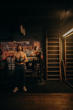 Athletic man in gym holding boxing gloves, showcasing strength and fitness.