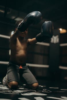 A young boy kneels in a boxing ring with gloves, showcasing determination and strength.