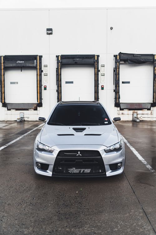 Free Silver sedan parked in front of industrial loading docks, showcasing modern car design. Stock Photo