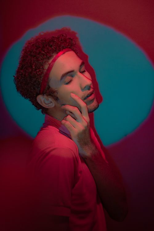 Free A young man with closed eyes poses creatively under a dramatic and colorful spotlight. Stock Photo