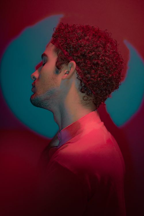 Free Artistic portrait of a man with curly hair, eyes closed under dramatic red lighting. Stock Photo