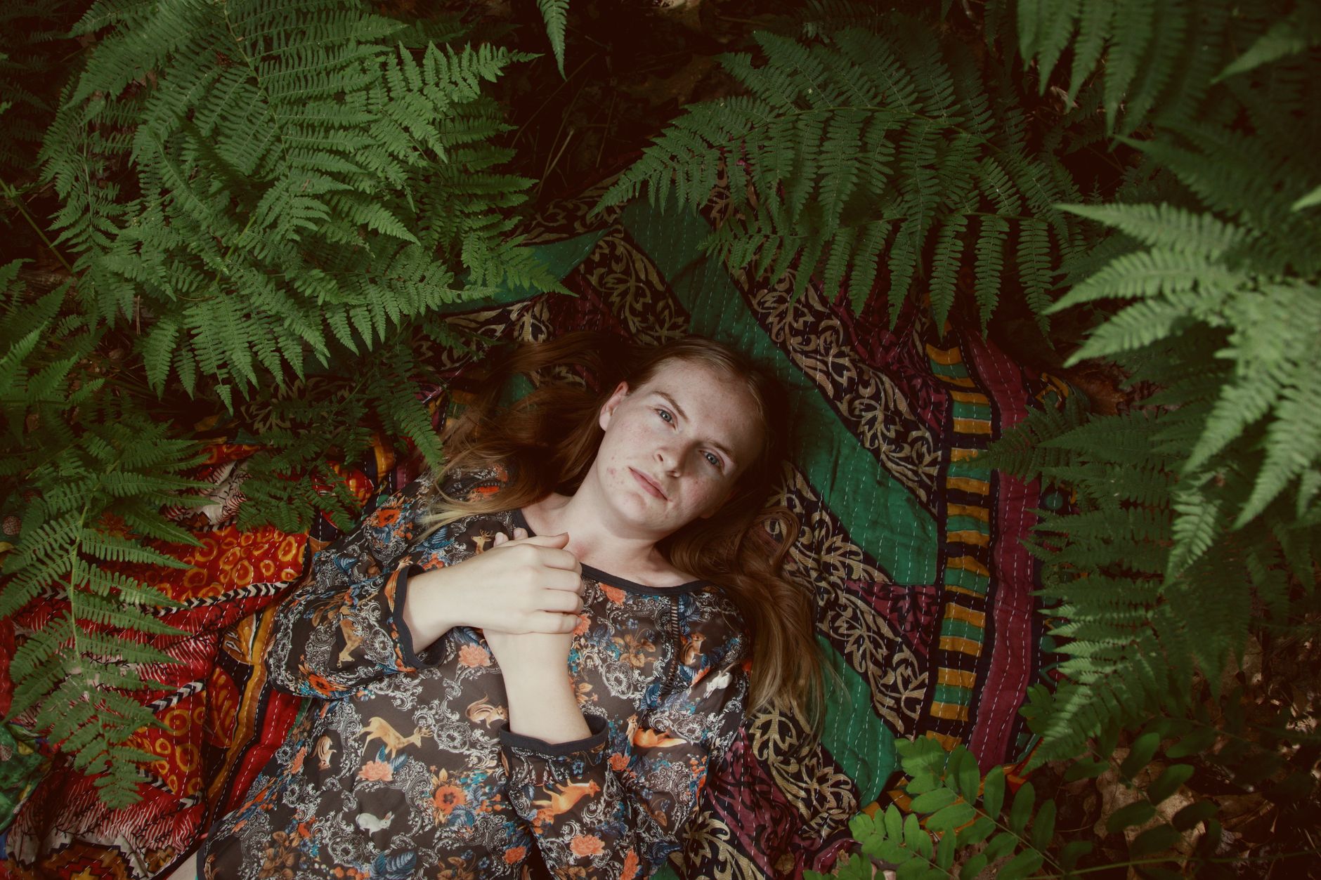 A woman lies peacefully on a vibrant blanket surrounded by lush green ferns.