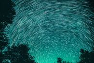 碧绿的天空中，星轨形成了令人惊叹的图案，前景里是树木的轮廓