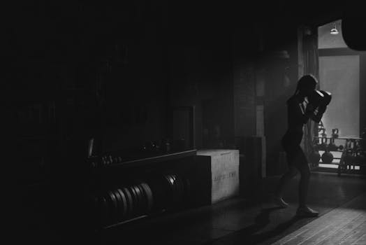 Silhouette of a woman shadowboxing in a dimly lit gym, emphasizing strength and focus.