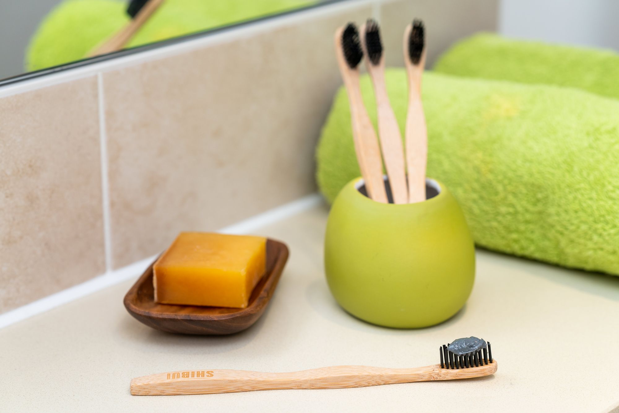 Bamboo toothbrushes, natural soap and a green towel arranged in a bright sustainable bathroom routine