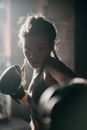 在光线昏暗的健身房里，专注的女拳击手正在出拳