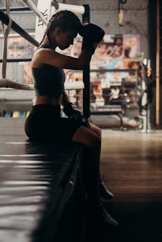 Side profile silhouette of a female boxer resting in an urban gym setting.