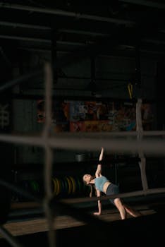 Woman engaging in a dynamic stretch exercise in a dimly lit gym setting, showcasing strength and flexibility.