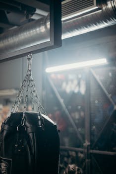 A dimly lit gym featuring a suspended black punching bag and industrial decor.