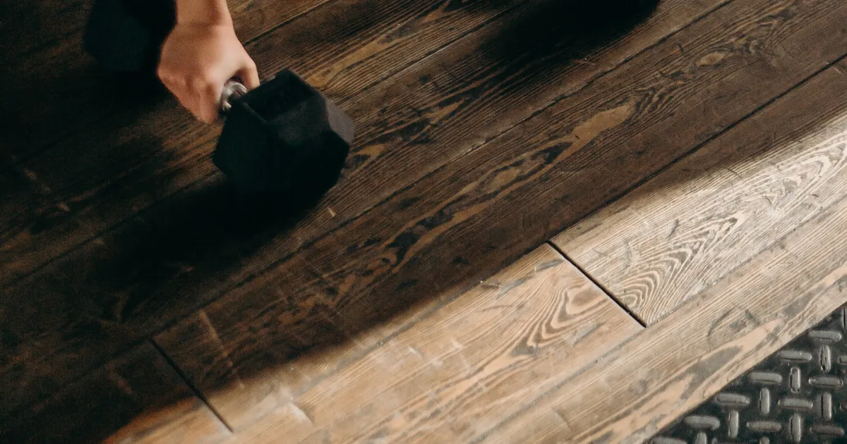 A hand picking a hex dumbbell up off a wooden floor
