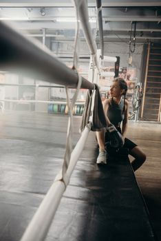Woman boxer sitting in a boxing ring with gloves and looking thoughtful, post-training.
