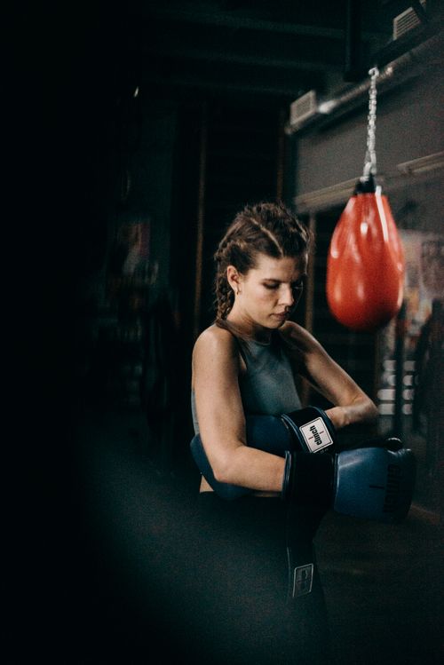 Free Female boxer putting on gloves preparing for intense training session in the gym. Stock Photo