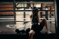 一名女拳击手在健身房擂台上休息，锻炼后用毛巾擦干汗水