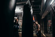 在一场重点拳击训练课程中，教练和运动员在室内与出气筒一起训练