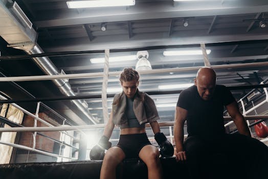 A female boxer and her coach take a break in the boxing ring, showcasing determination and focus.