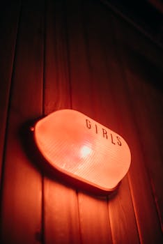 A close-up of a glowing red sign labeled 'Girls' mounted on a wooden wall, indoors.