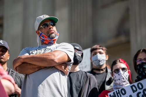 Free Serious African American man in glasses and casual clothes standing on street near protesting crowd during pandemic Stock Photo