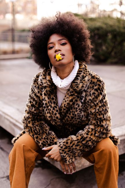 Stylish woman in New York with afro hair wearing leopard print coat, posing with yellow flower.