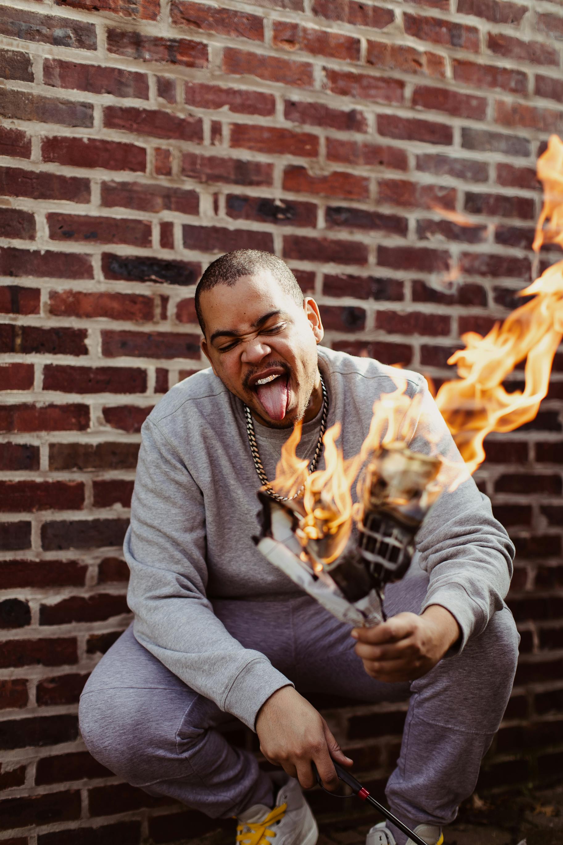 Dynamic photo of a man squatting near a brick wall, holding a flaming microphone.