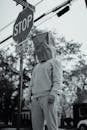 Grayscale Photo of Man in Jacket Standing on Stop Sign