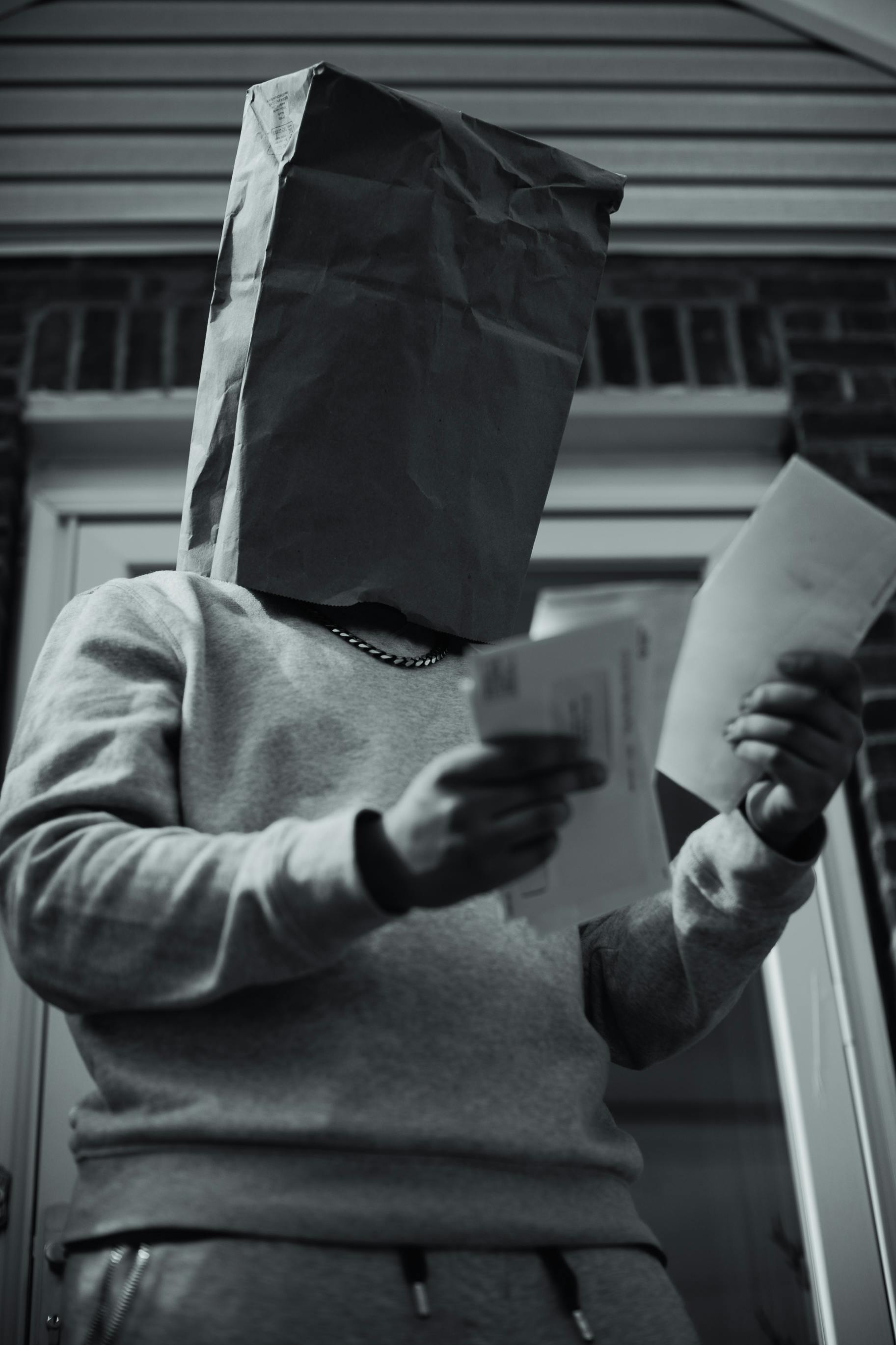 person with paper bag on head holding envelopes
