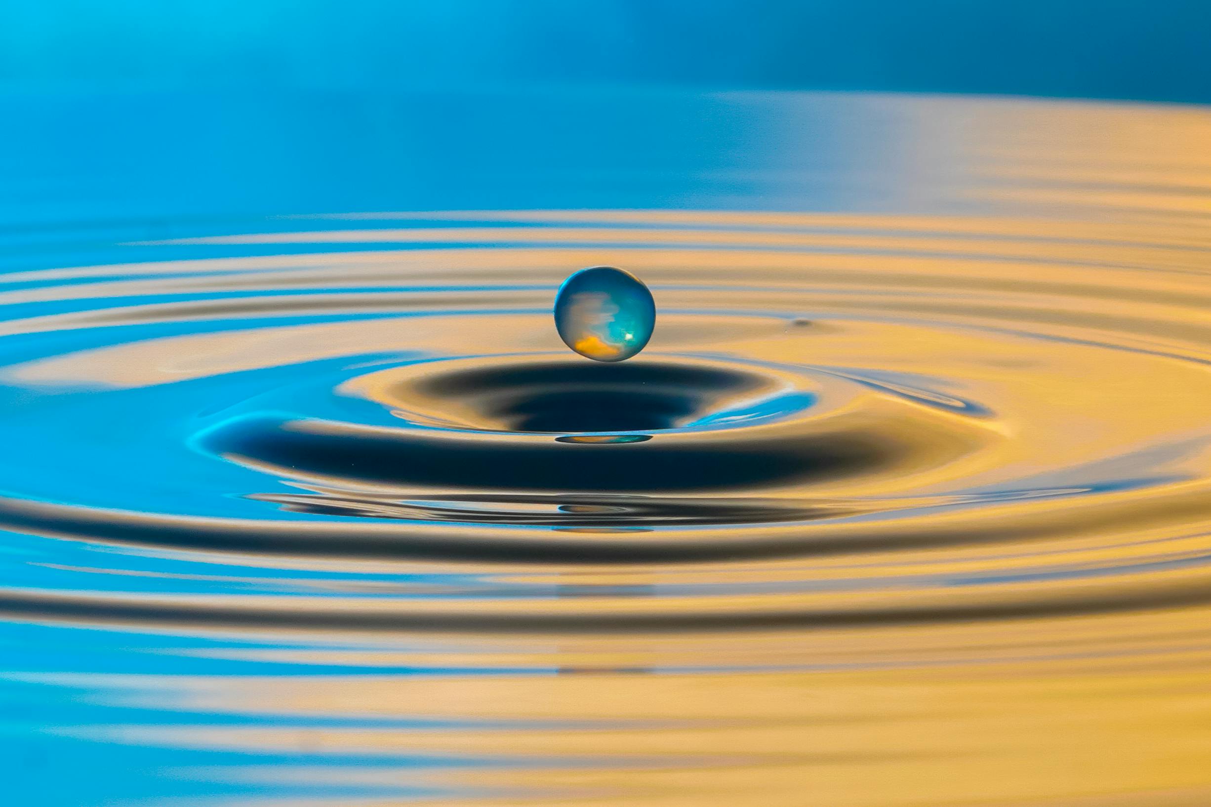 Stunning capture of a water droplet suspended mid-air over rippling water, highlighting nature