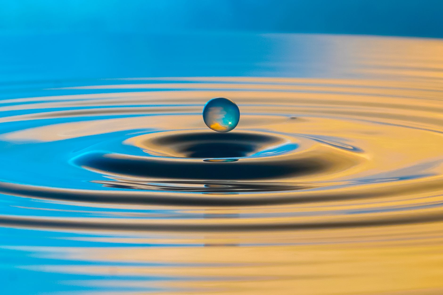 Stunning capture of a water droplet suspended mid-air over rippling water, highlighting nature's beauty.