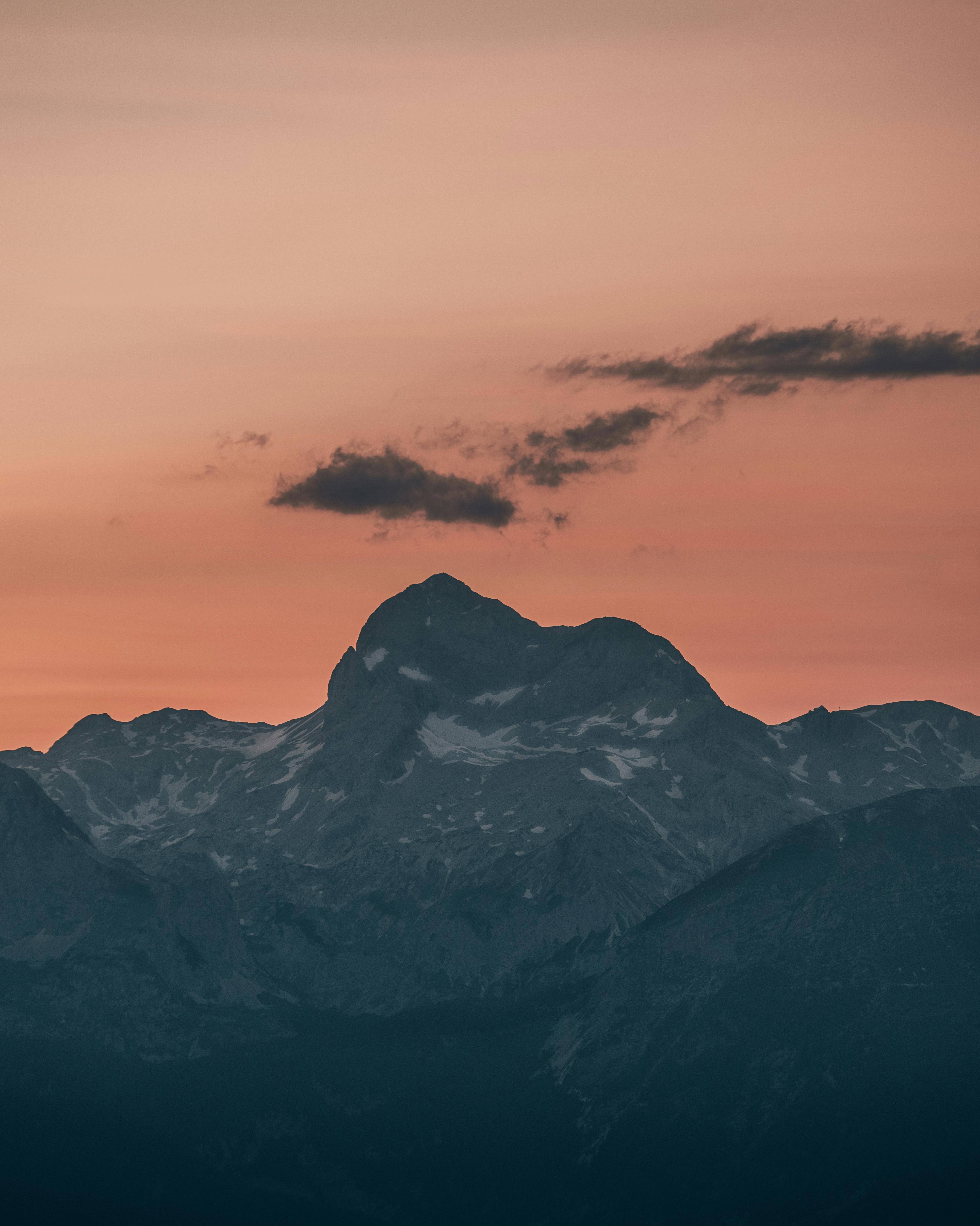 Capture the serene beauty of Slovenian mountains during twilight, framed against a warm orange sky.