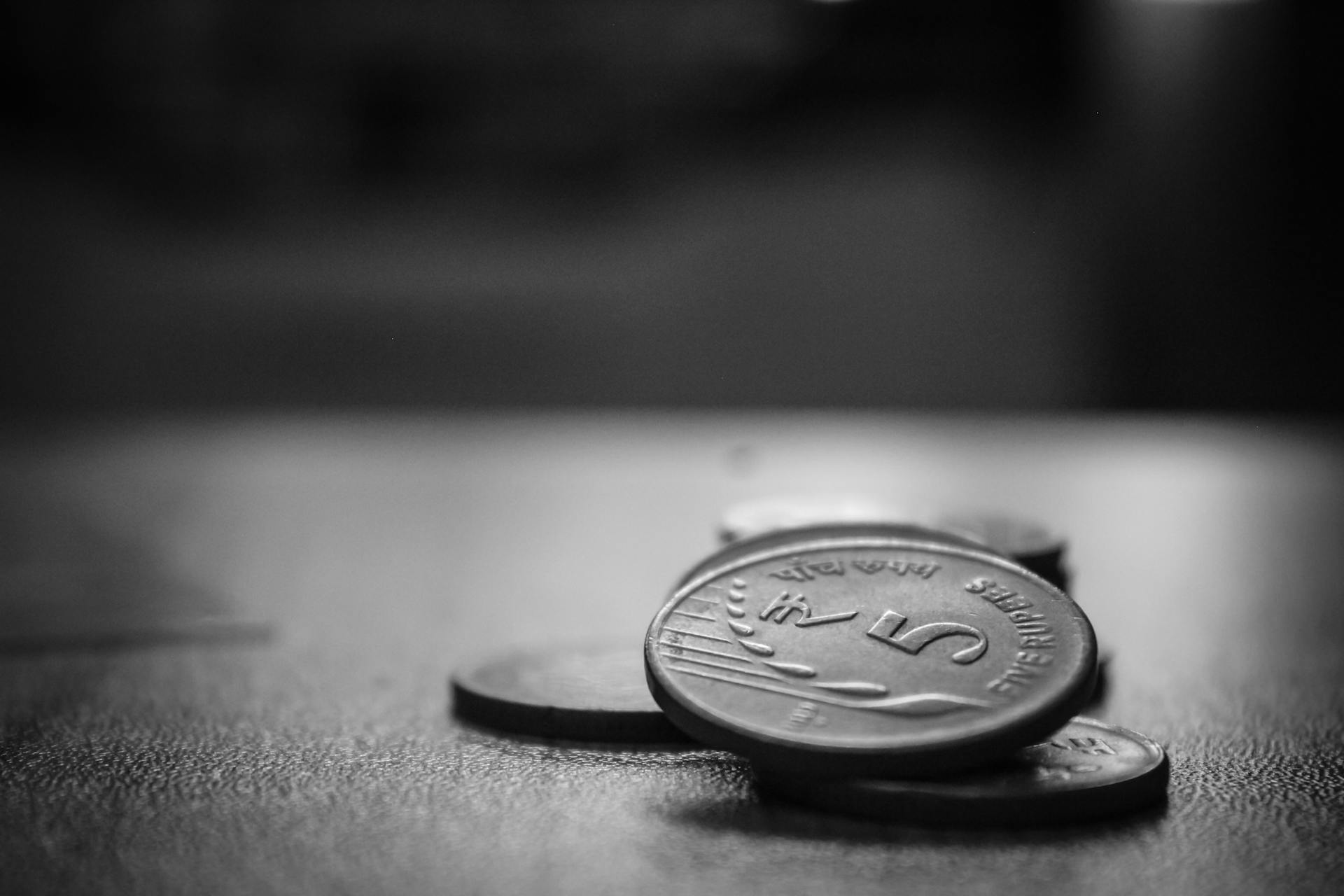 A monochromatic close-up of Indian five rupee coins stacked on a surface, emphasizing texture.