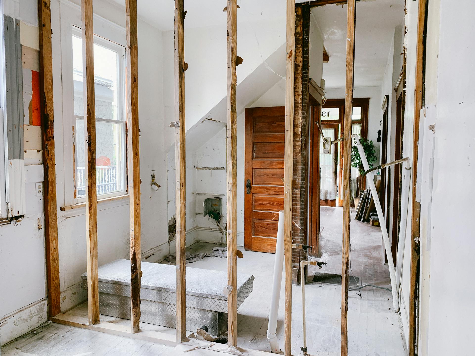 Interior view of a home under renovation with exposed wooden beams and door.