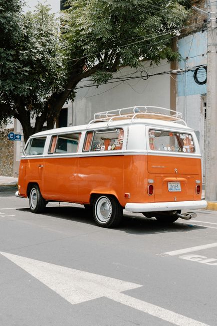 Vintage orange Volkswagen van parked on a city street with trees nearby, showcasing a nostalgic vibe.