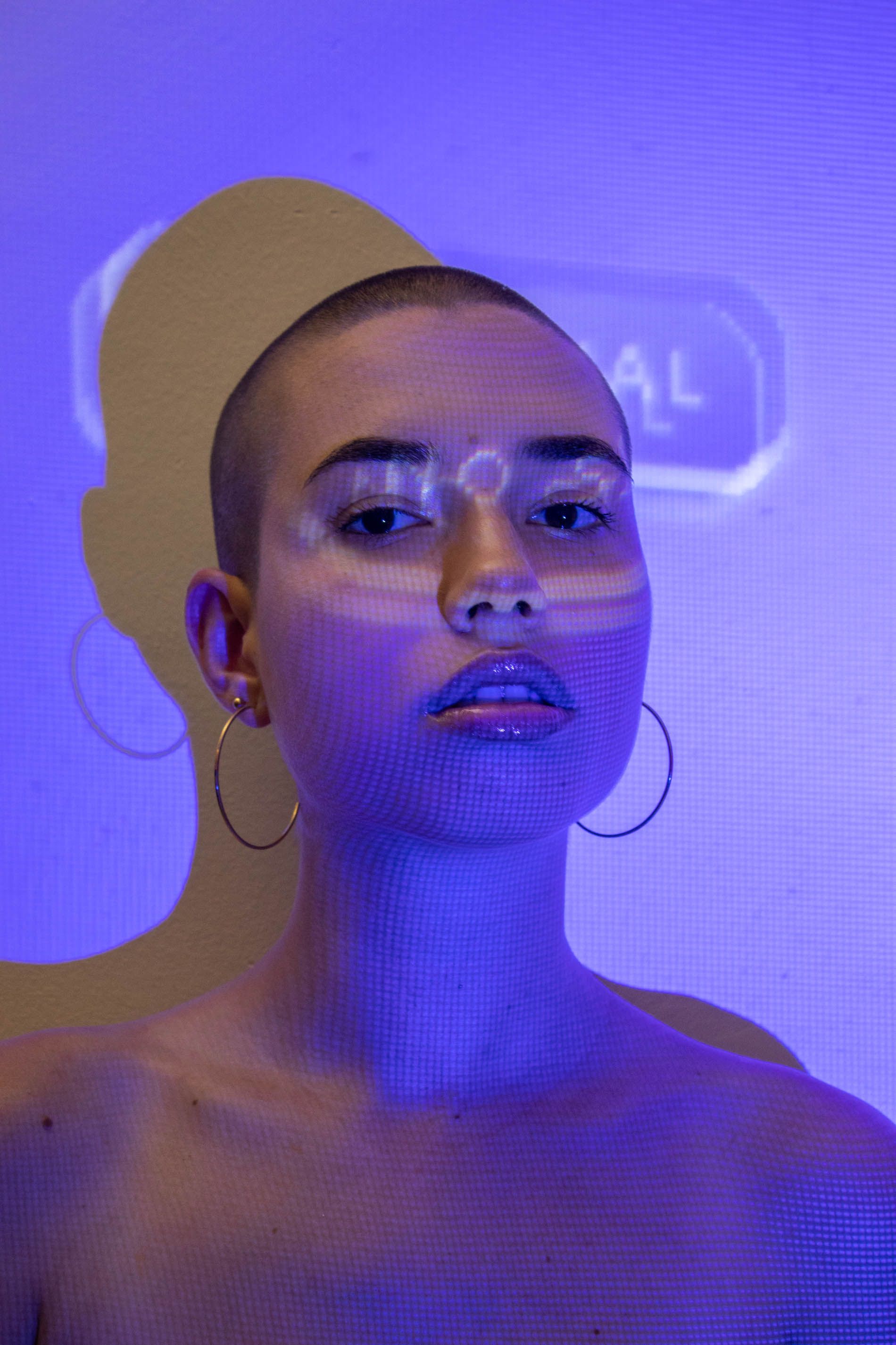 Portrait of a woman with hoop earrings under a blue light projection creating a unique effect.