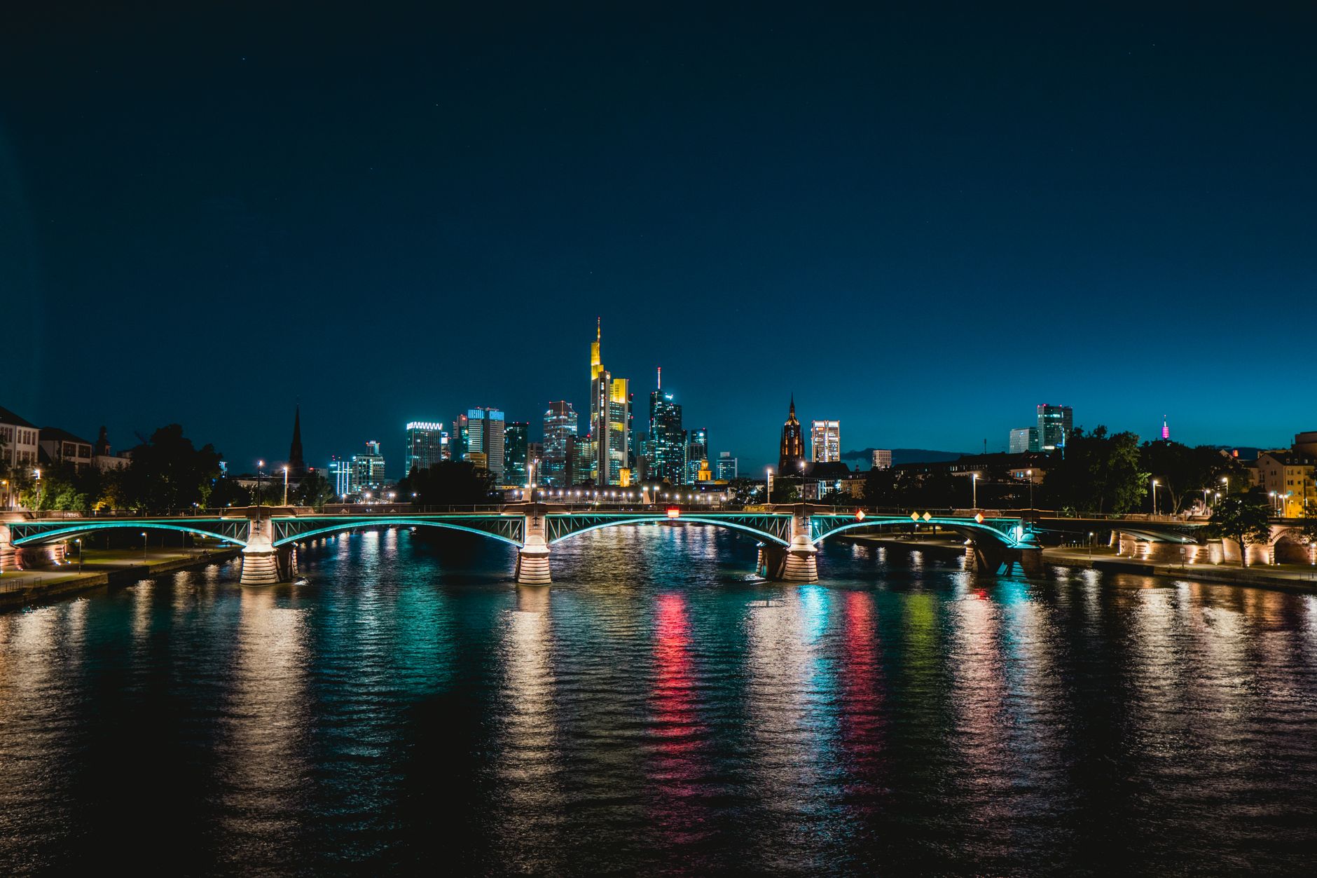 Stunning night view of Frankfurt's skyline and reflections on the river with illuminated bridge.