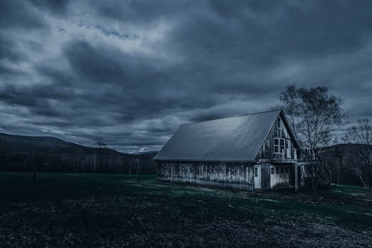 A weathered wooden barn in a rural setting beneath a dramatic, cloudy sky.
