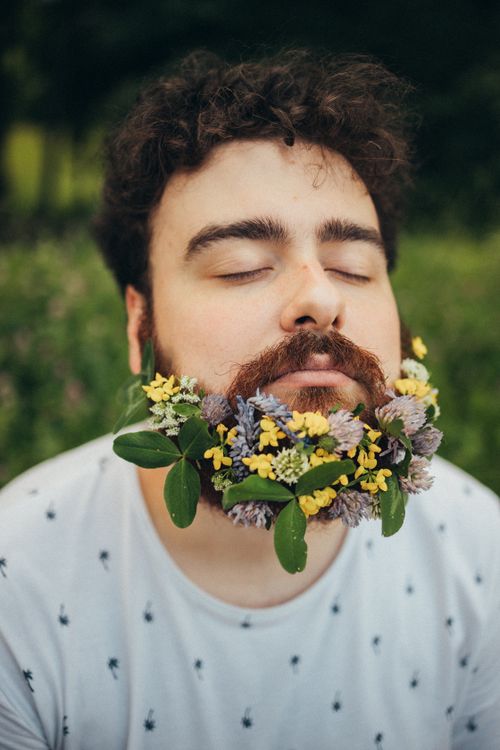 Free A serene man with a floral-decorated beard, eyes closed, in nature. Stock Photo
