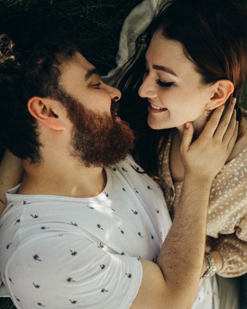 Free A couple enjoys a joyful, intimate moment lying on grass on a sunny day. Stock Photo