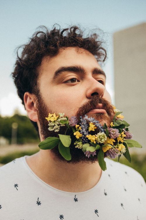 Free Portrait of a young man with flowers in his beard, exuding a nature-inspired style. Stock Photo