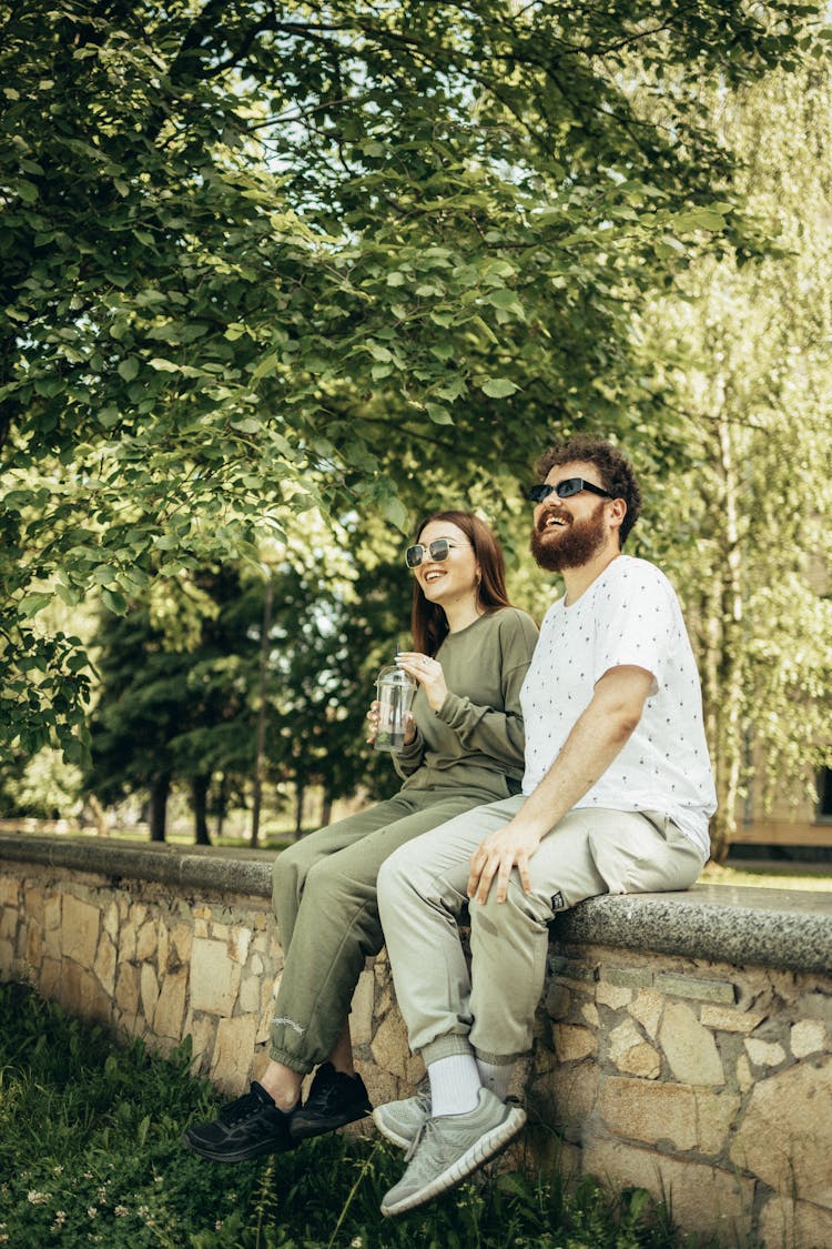 Man And Woman Sitting On Concrete Bench Near Green Tree