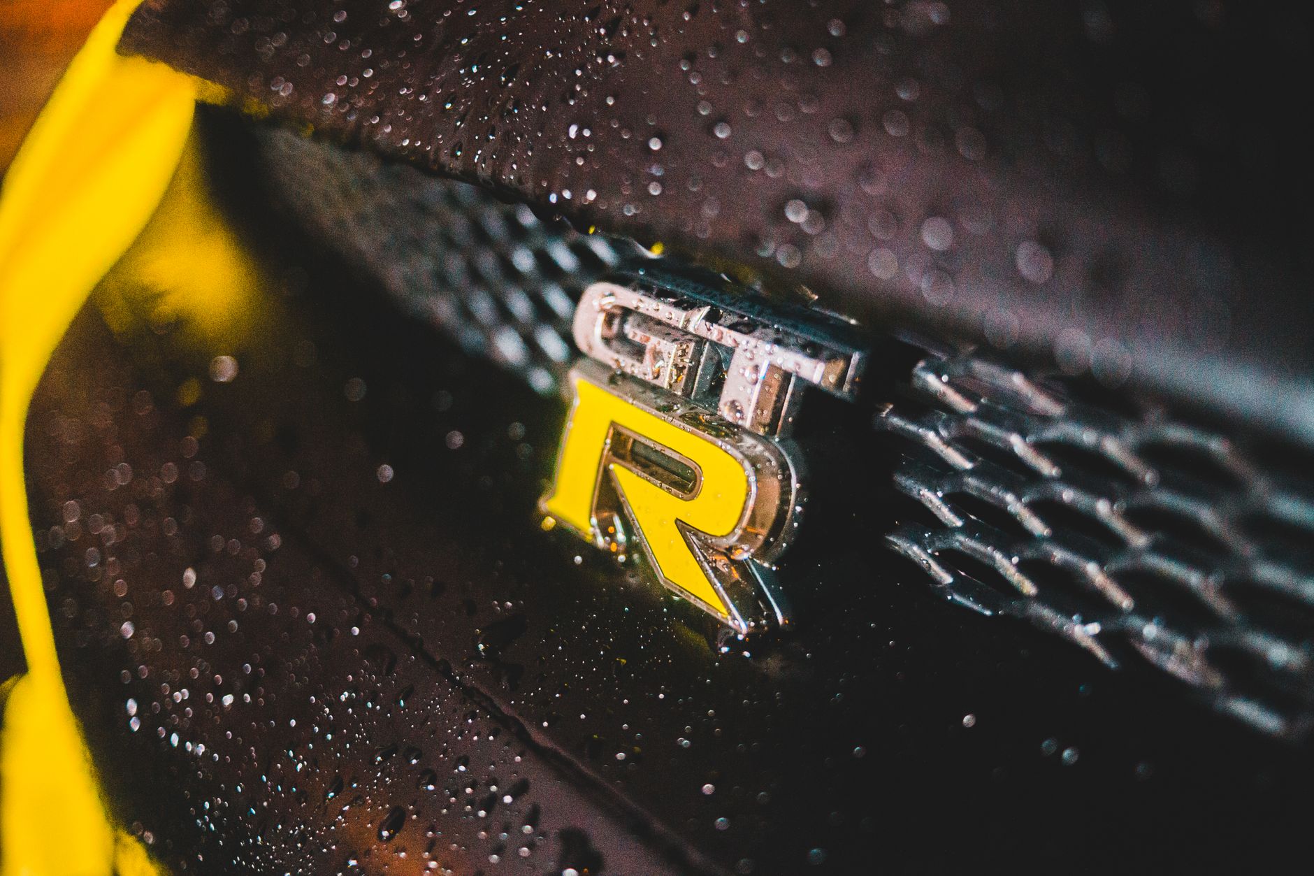 Closeup of luxury yellow detail on black wet automobile on street in rainy weather