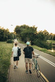 Two young adults strolling on a path with a bicycle, surrounded by lush greenery.