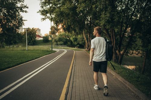 Free A man walks through a peaceful park on a paved path surrounded by lush greenery. Stock Photo