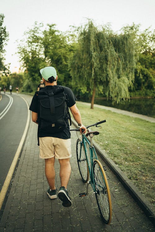 A Man Walking on Sidewalk While Holding a Bicycle